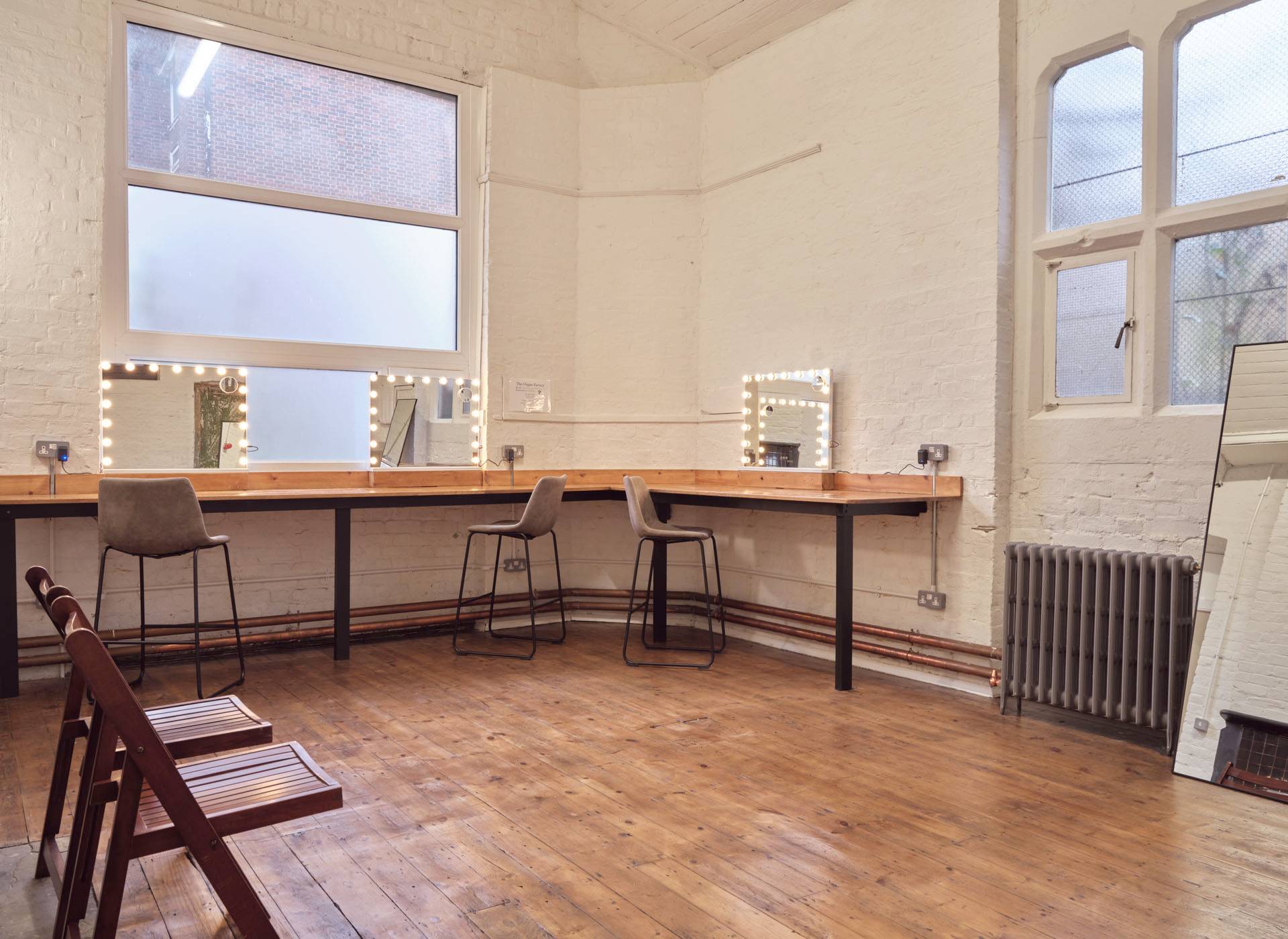 Dedicated hair and makeup suite featuring a long wooden vanity counter, illuminated makeup mirrors, and bar stools, ideal for fashion shoot prep, Love Locations.