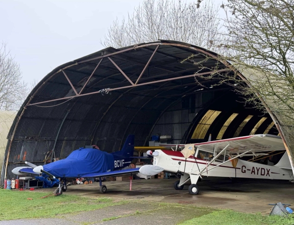 Open curved aircraft hangar showing parked planes on a historic World War era airfield site in Corby, NN17, Love Locations.