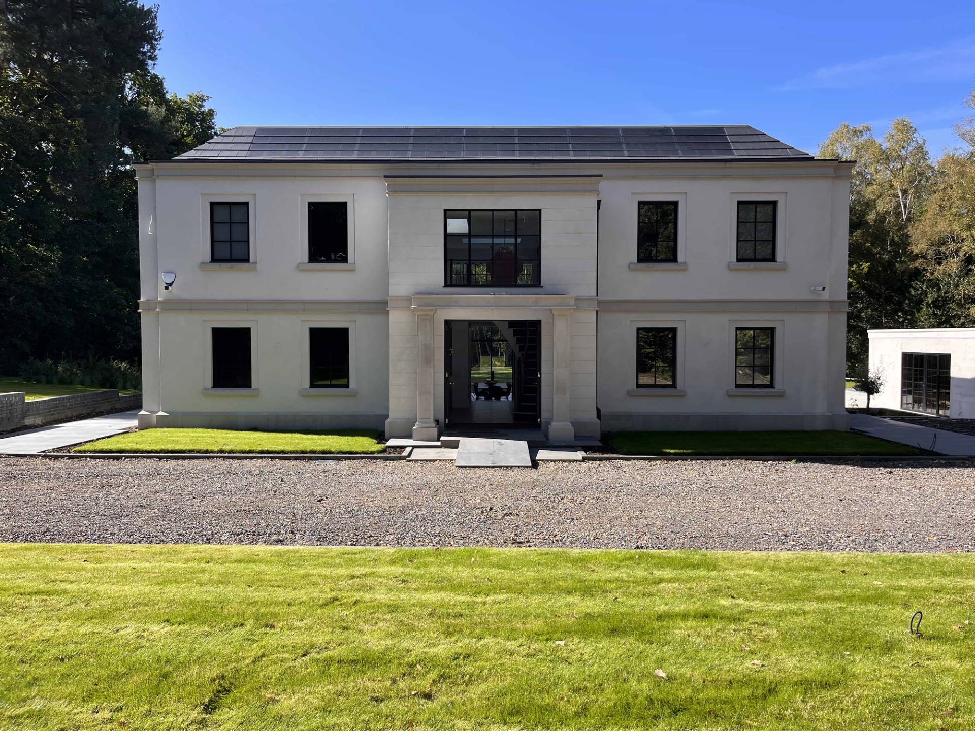 Modern neo-classical mansion front exterior shoot location in Surrey, GU3 featuring a grand portico entry, gravel driveway, and white rendered facade, Love Locations.