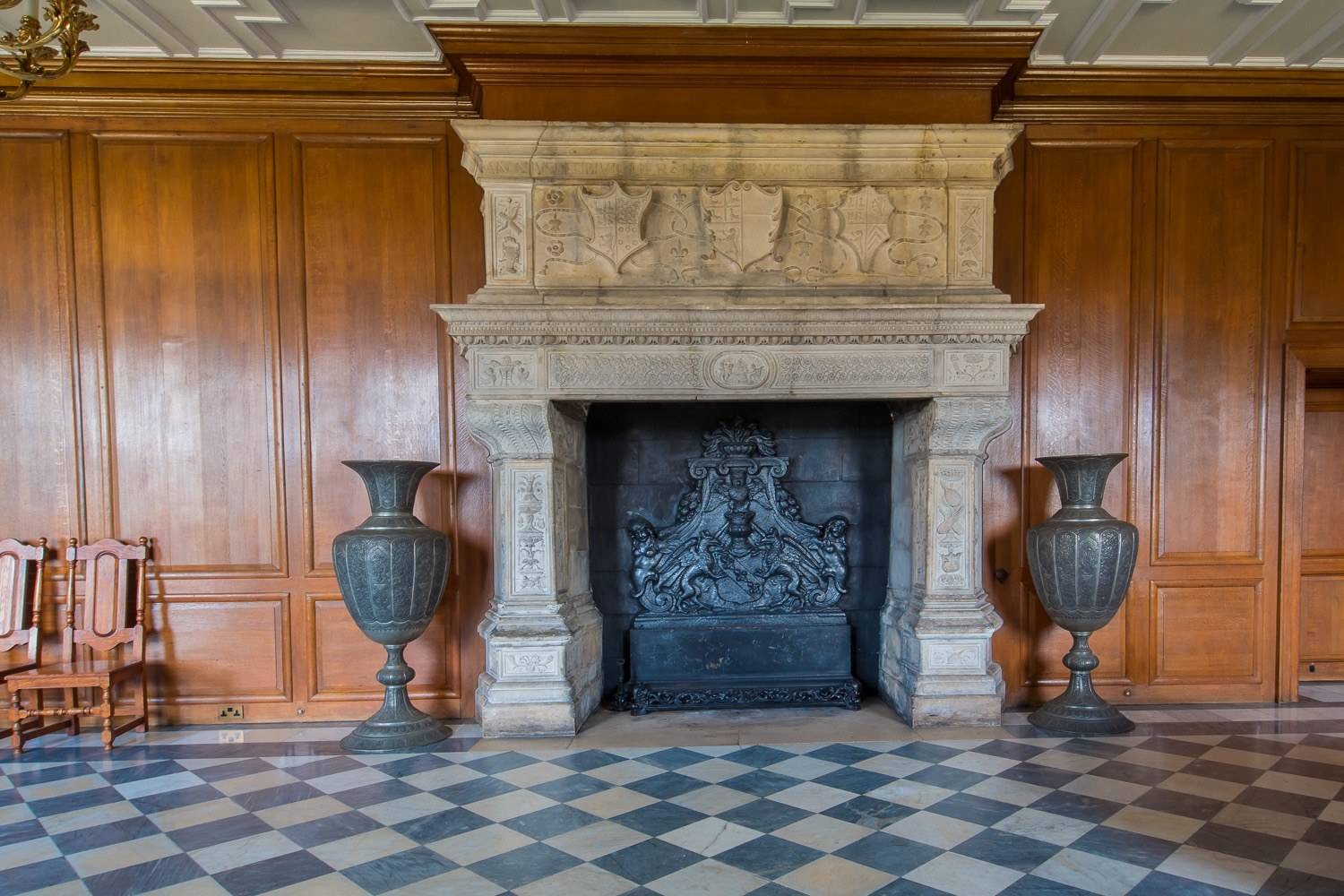 Carved Elizabethan stone fireplace and ornamental urns set against wood-panelled walls in a Hertfordshire country estate shoot space by Love Locations.