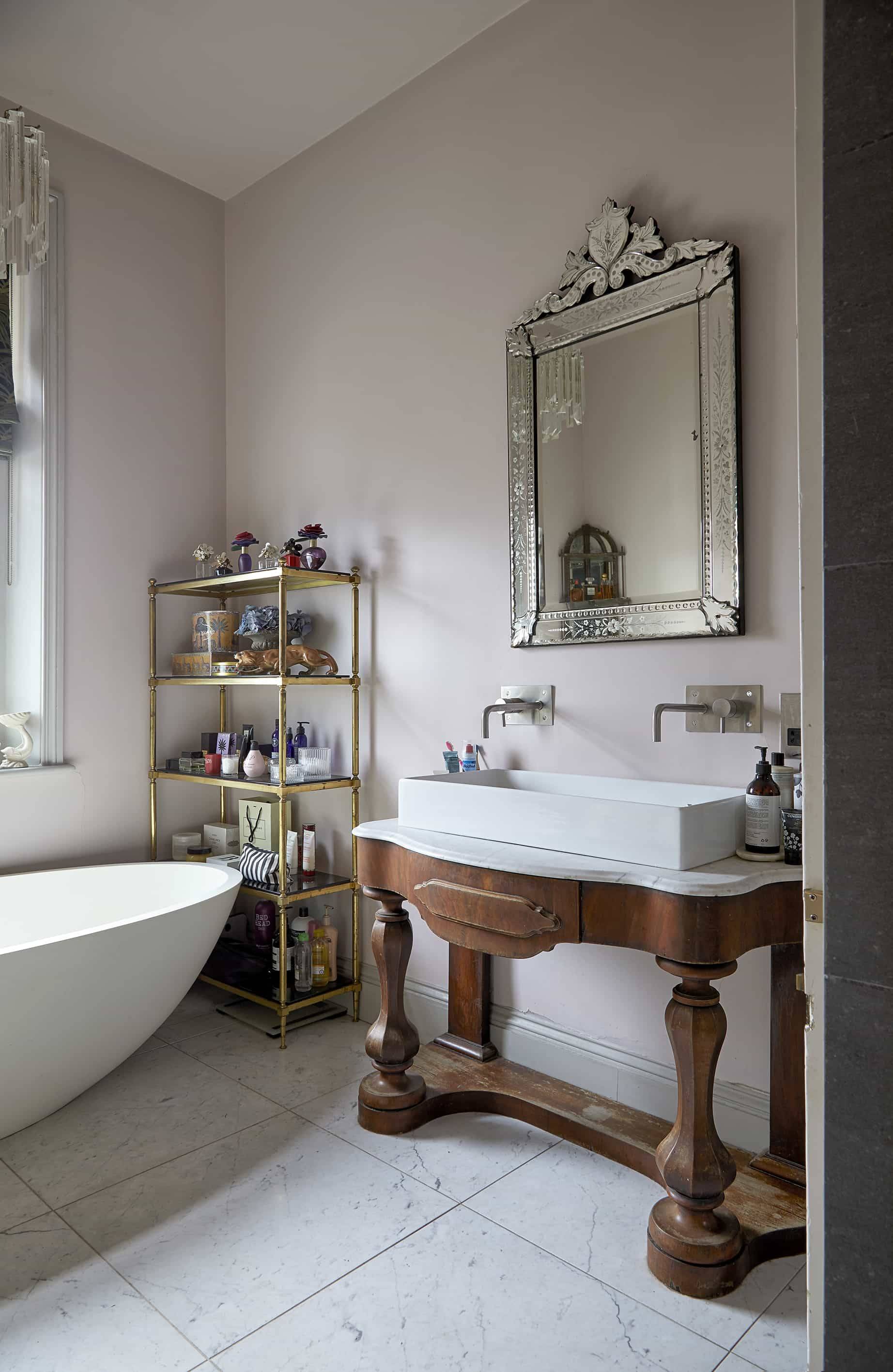 Bathroom vanity setup with a wooden vanity unit, white sink, and arched ornate mirror beside a soaking tub, Love Locations N16.