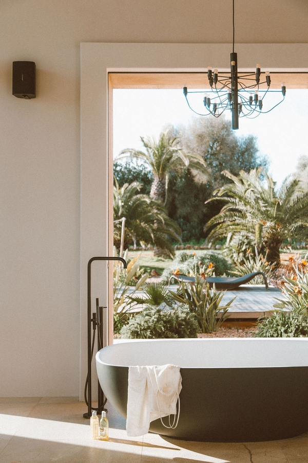 Luxury bathroom view framing a freestanding bathtub set in front of floor-to-ceiling garden windows, Love Locations 07630.