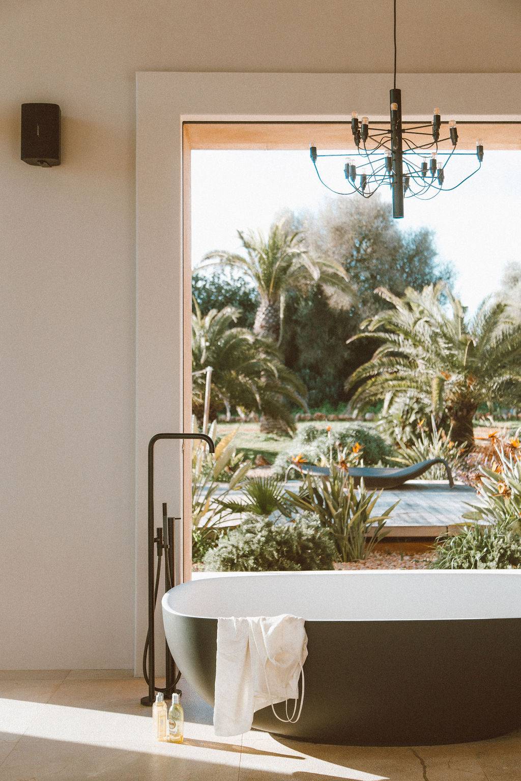 Luxury bathroom view framing a freestanding bathtub set in front of floor-to-ceiling garden windows, Love Locations 07630.