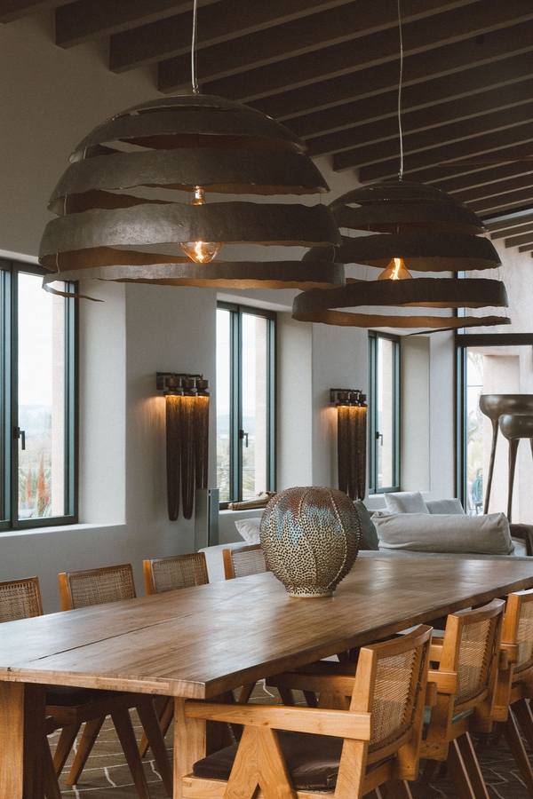 Long wooden dining table layout framed by oversized metal pendant lamps and floor-to-ceiling windows, Love Locations 07630.
