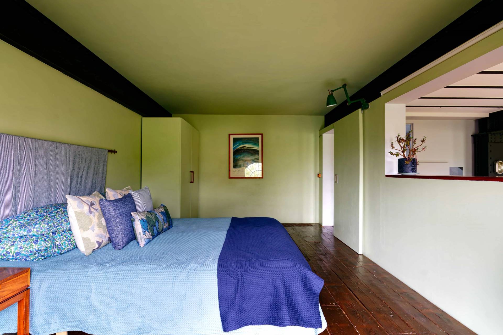 Minimalist loft bedroom with sage green painted walls, dark timber flooring, and simple double bed arrangement, Love Locations E14.