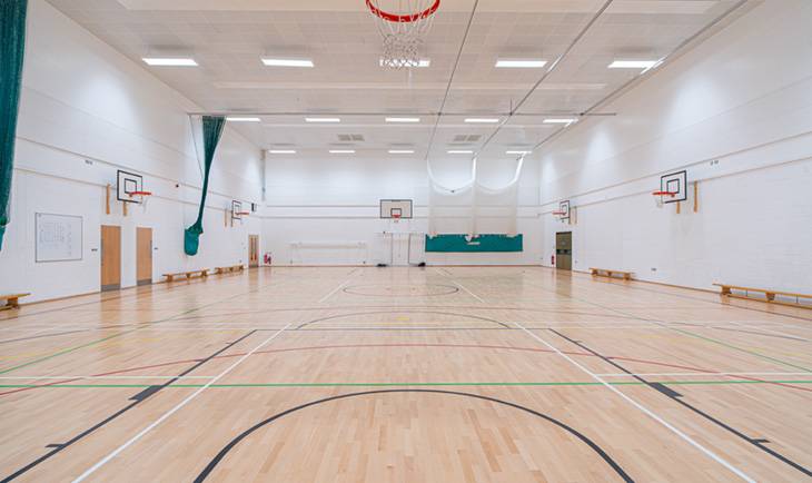 Wide view of a large multi-court school gymnasium shoot space with sports equipment and tall ceiling rafters from Love Locations.