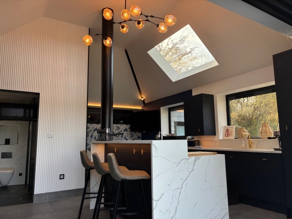 Modern vaulted ceiling pool house studio in Essex CM4 from Love Locations, displaying a white marble island, black bar stools, high ceilings, and skylights.