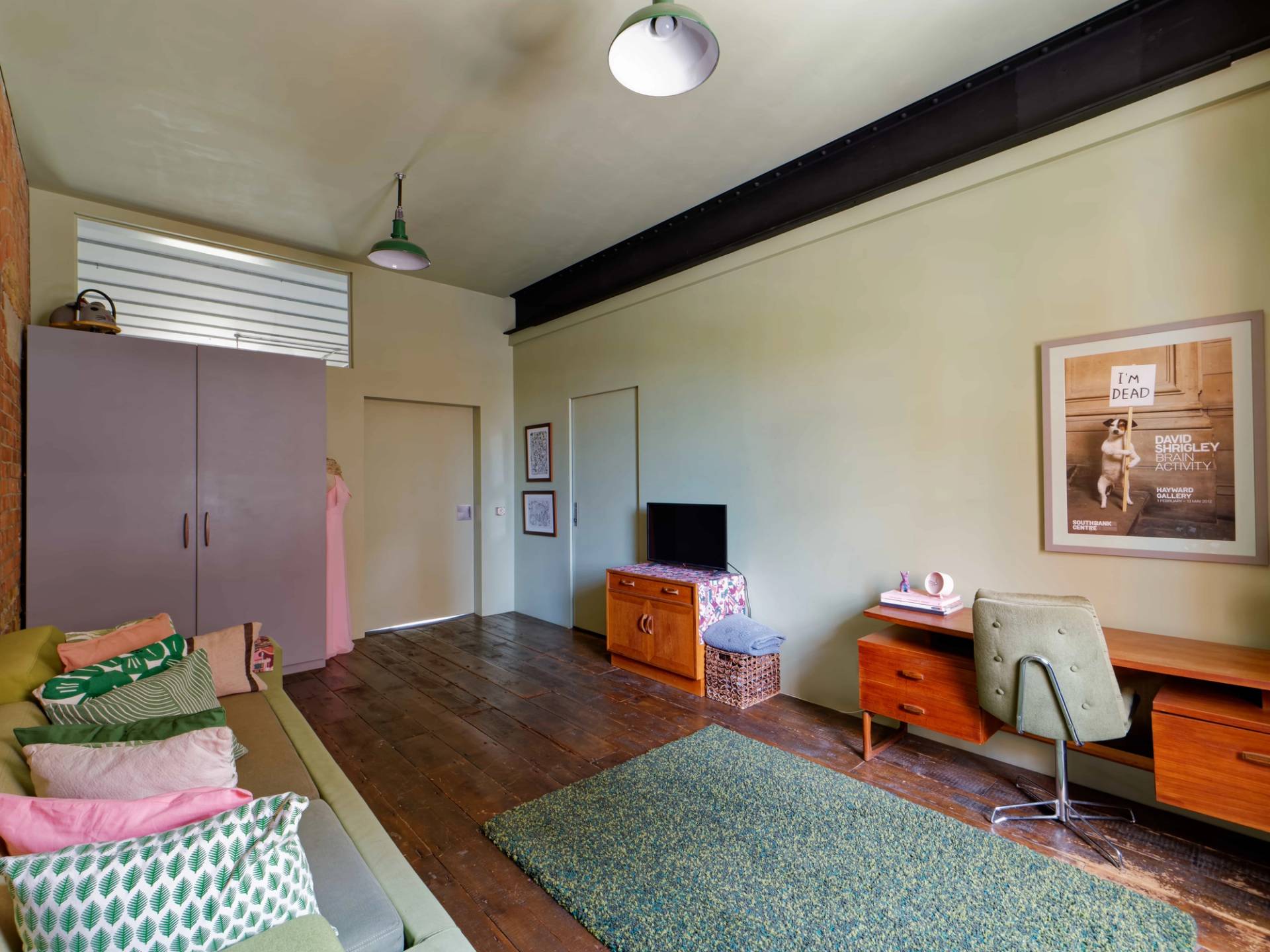 Loft sitting area featuring a green sofa bench set against exposed red brick walls and sage green rug, Love Locations E14.