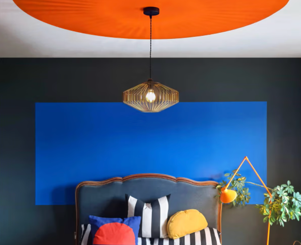 Colour-drenched bedroom at Drakeford with bold blue feature wall, orange ceiling circle and graphic striped bedding.