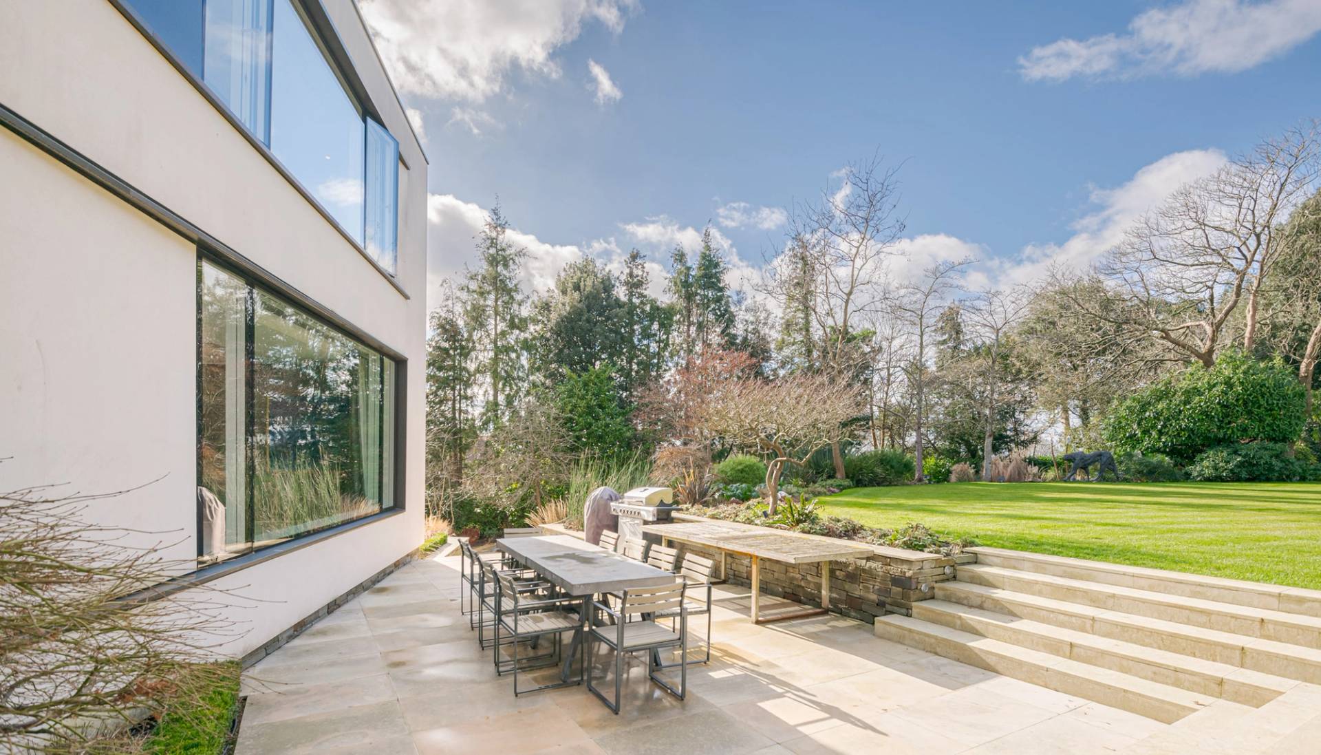 Outdoor dining terrace set with modern grey outdoor furniture overlooking a landscaped garden, Love Locations KT2.