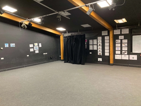 Love Locations black box drama studio film location CM1: Atmospheric performing arts rehearsal room with deep grey walls, blackout curtains, and an industrial overhead studio lighting grid, perfect for indie film sets.