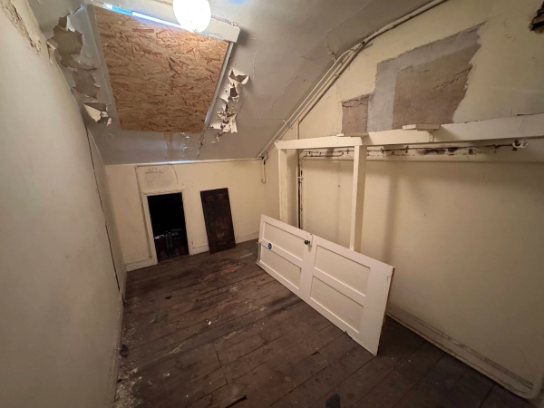Dilapidated attic storage space with sloped ceilings, loose door fixtures, and decaying plasterwork, listed by Love Locations.