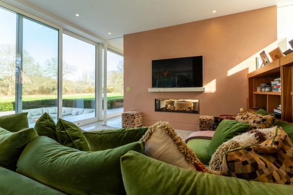 Love Locations atmospheric snug location Surrey GU8: Intimate living space centered around an integrated modern linear fireplace, a soft terracotta wall, and green velvet seating, excellent for movie sets.
