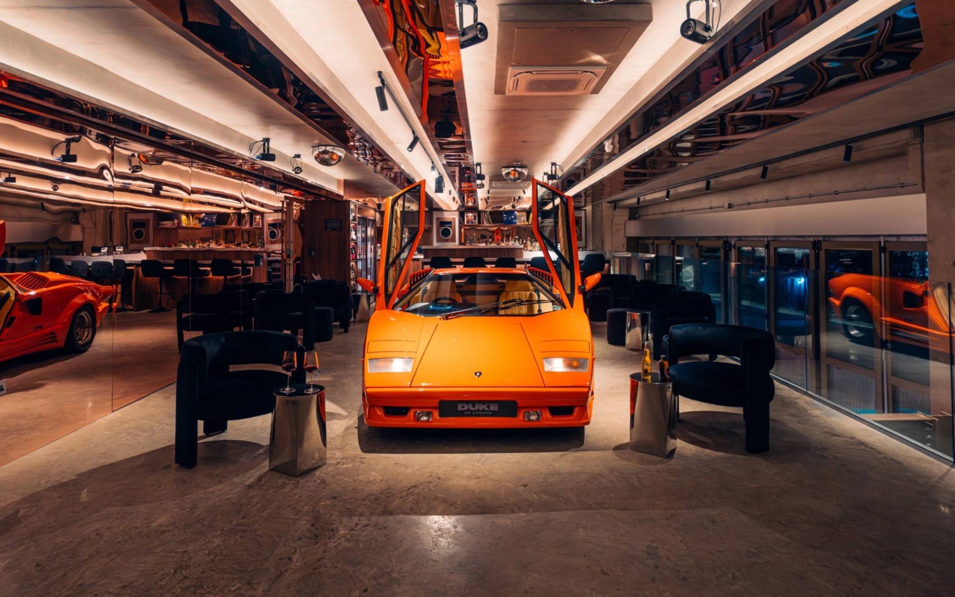 Symmetrical front view of an orange Lambo with raised scissor doors inside a venue space via Love Locations.