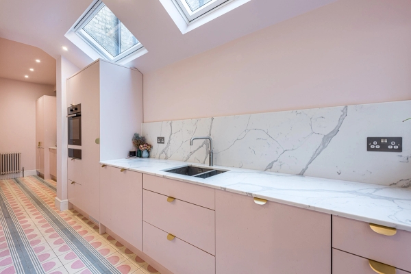 Minimalist kitchen sink run with luxury pink cabinetry, integrated brass handles, and marble splashback, curated by Love Locations.
