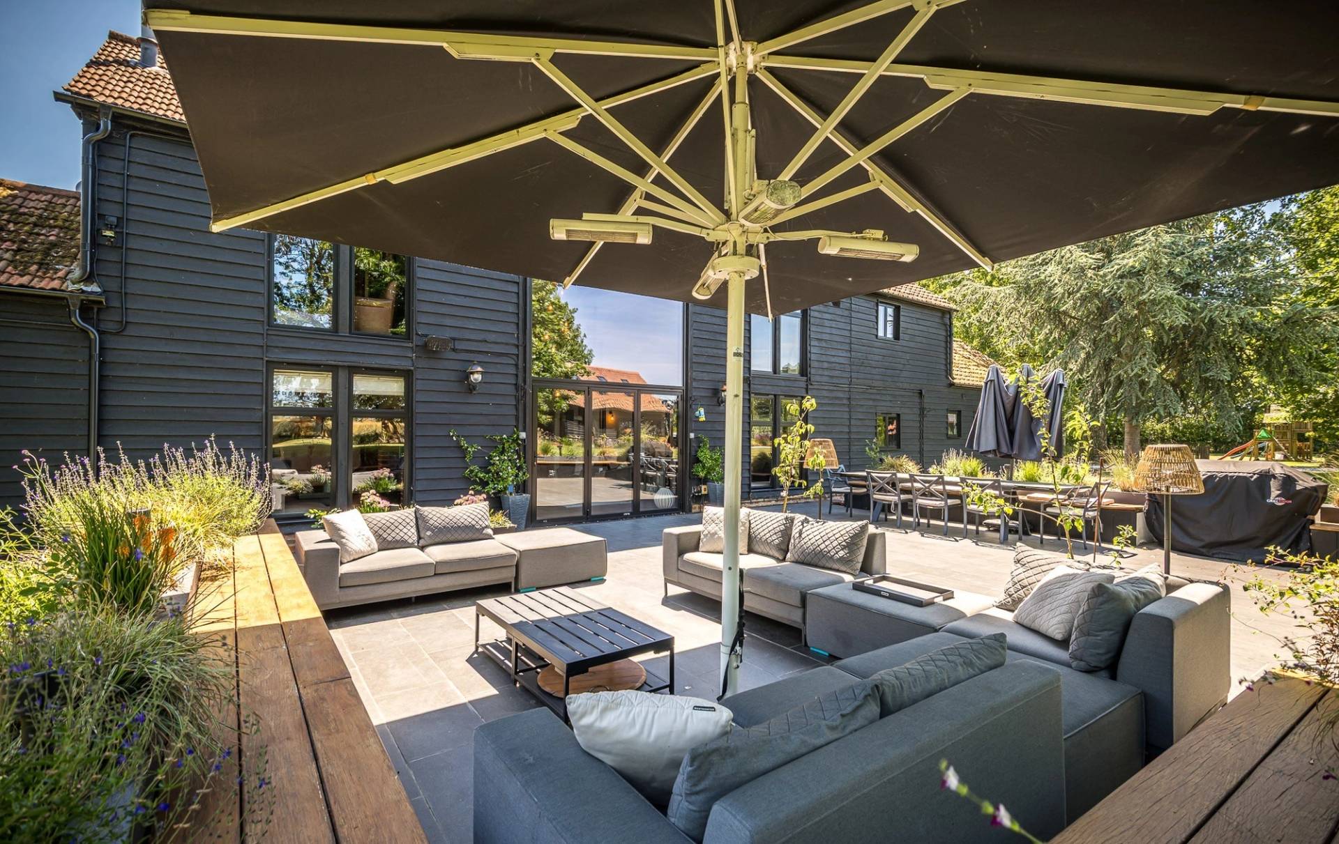 Luxury outdoor patio living space with a grey rattan corner sofa and large garden parasol umbrella, Love Locations CM3.