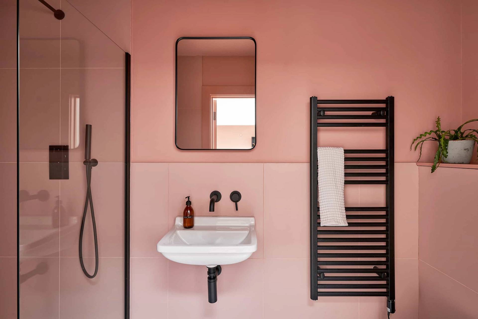 Terracotta pink wet room featuring a wall-mounted sink, black towel radiator, and arched mirror, Love Locations IP30.
