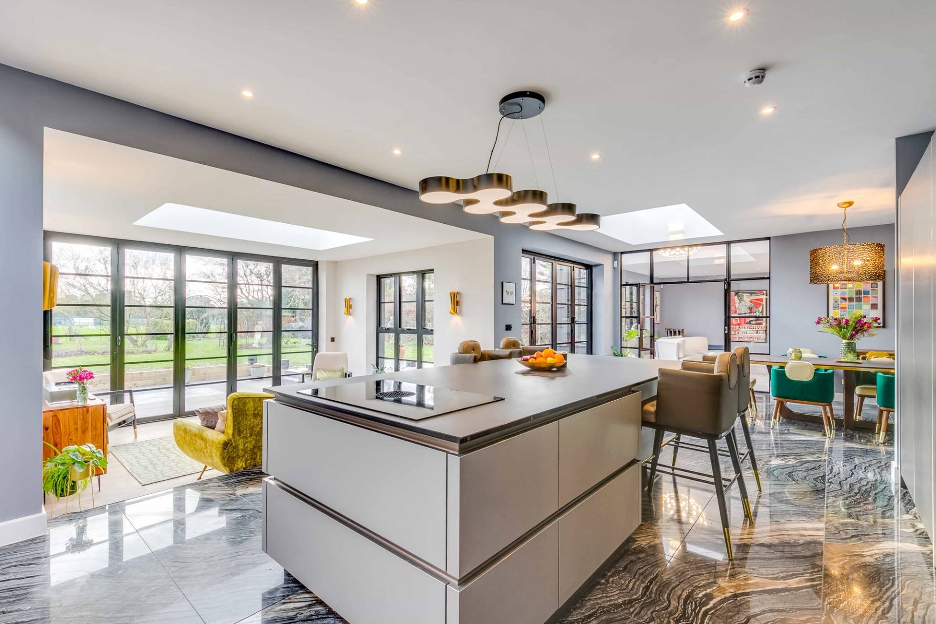 Kitchen view looking across a large island counter toward crittall doors and garden views, Love Locations CB2.