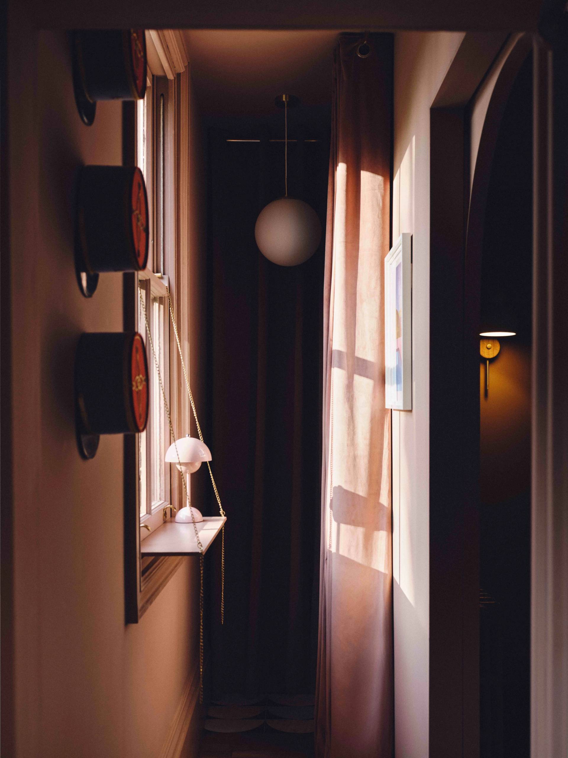 Plaster pink hallway detail showing dark wall sconce lights casting warm light onto timber floorboards, Love Locations CR0.