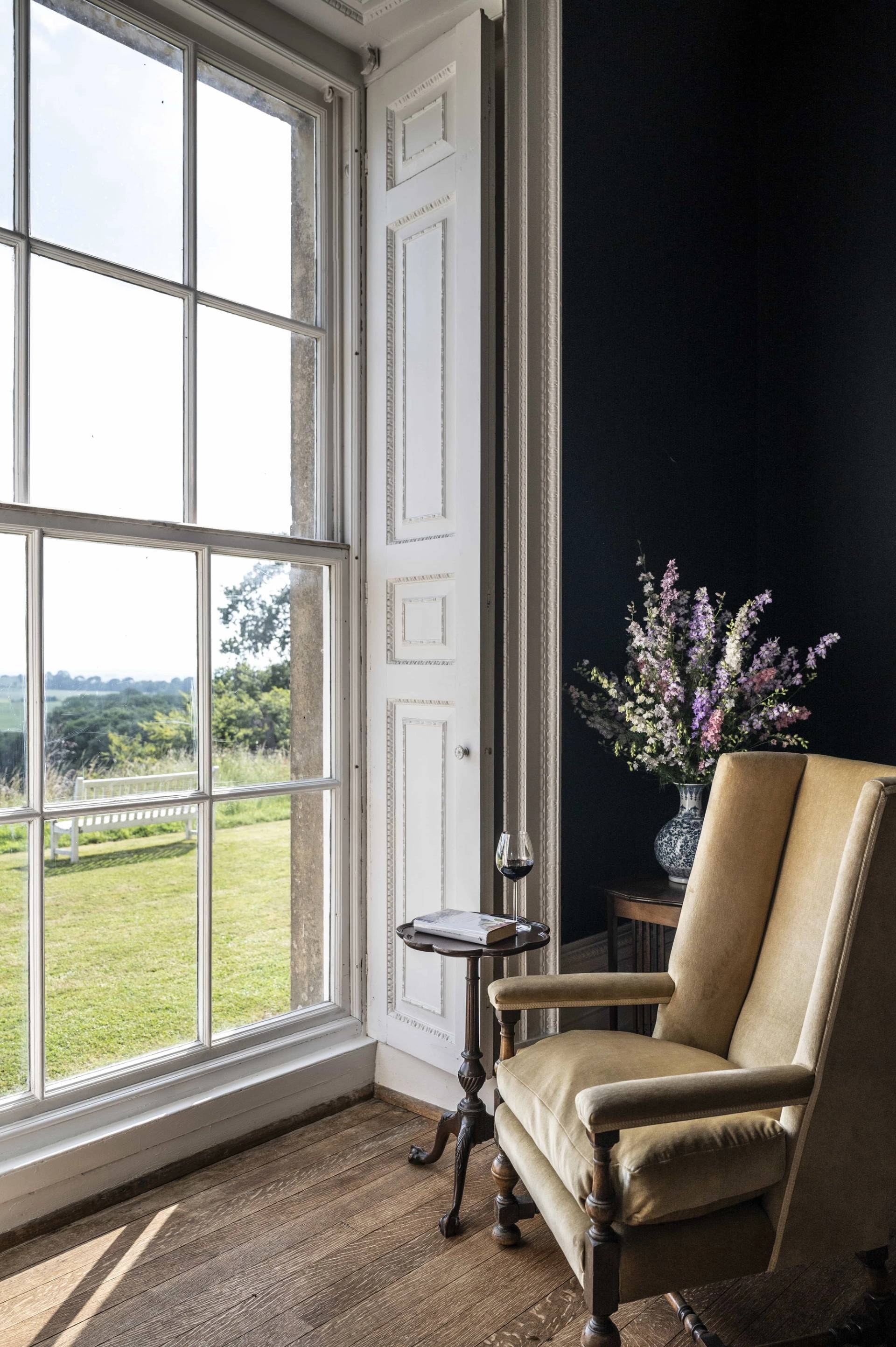 Neutral armchair sitting beside a tall sash window in a dark navy reception room in Tugby, Leicestershire, Love Locations LE7.
