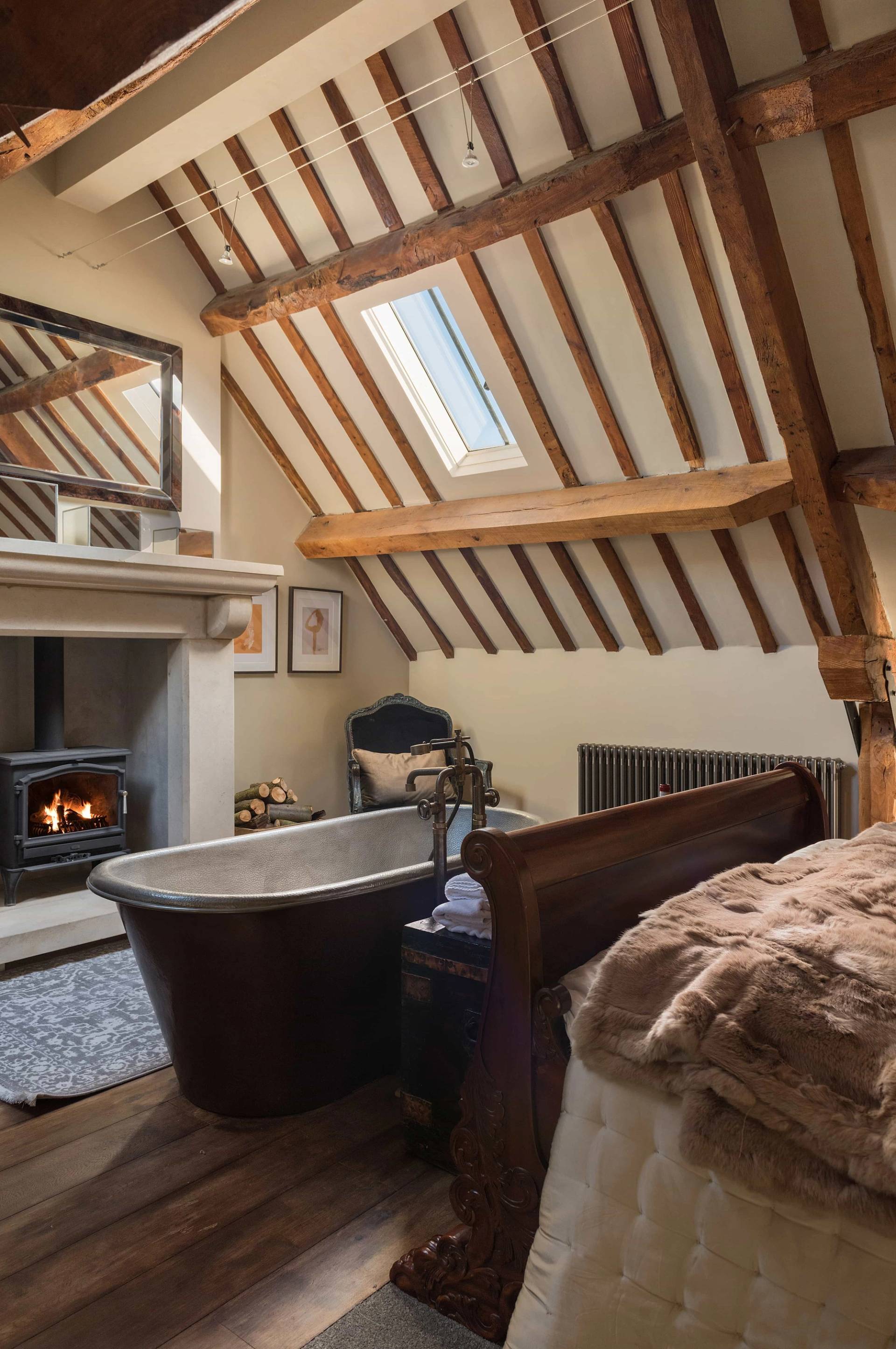 Luxury ensuite bedroom filming space through Love Locations, featuring an antique copper roll-top bathtub set beneath sloping wooden roof beams and skylights.