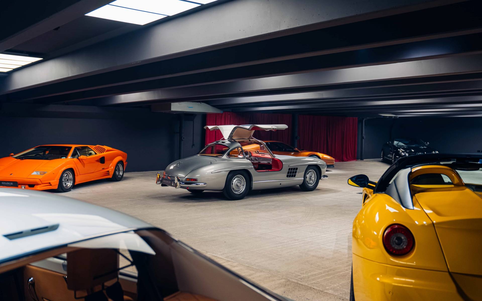 Silver Mercedes Gullwing sports car with raised doors inside a dark concrete underground vault by Love Locations.