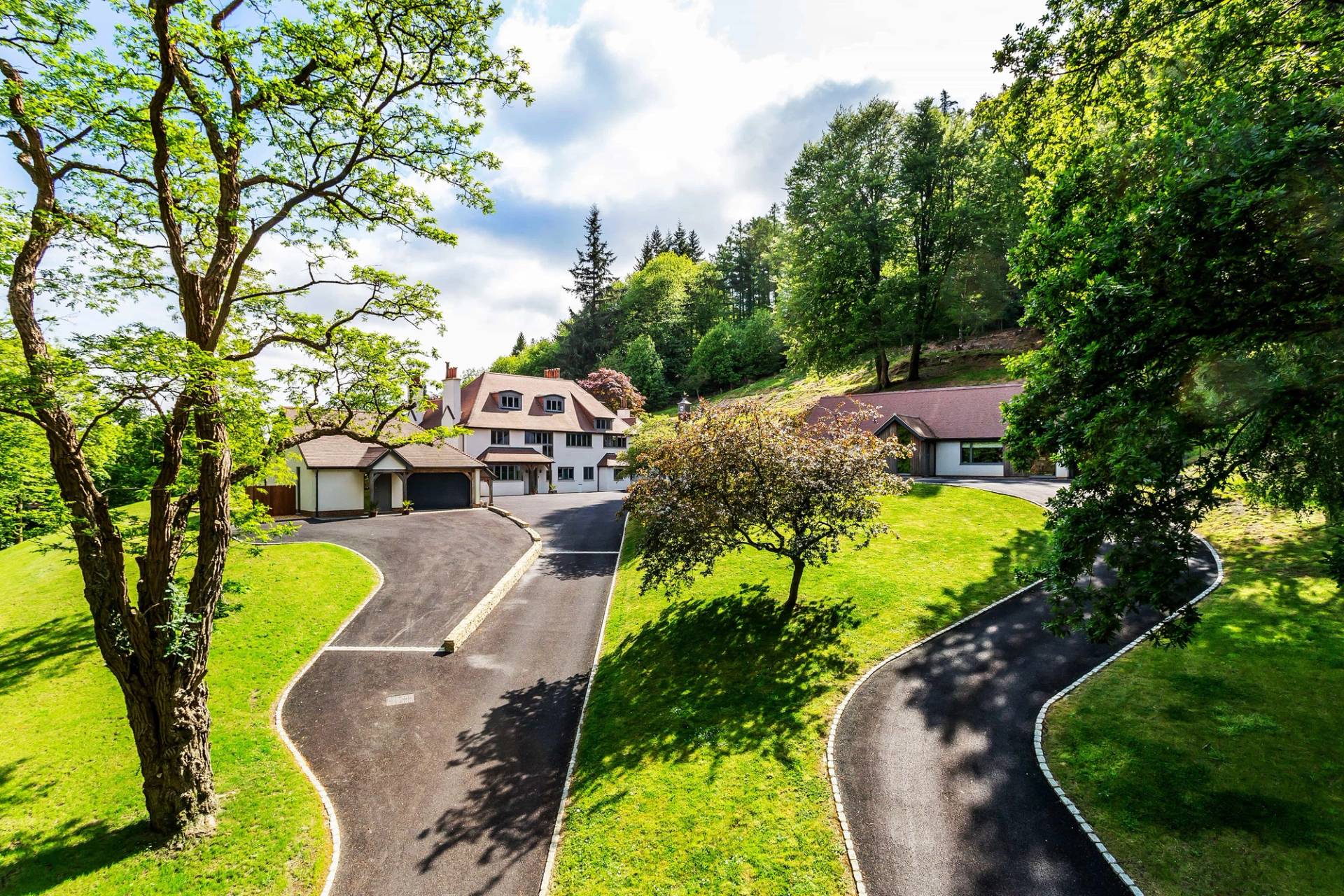 Aerial perspective of a detached country estate surrounded by rolling hills, manicured gardens, and dense woodland, Love Locations GU27.