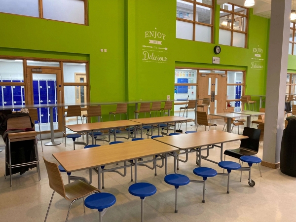 Love Locations bright school dining hall location CM1: Educational cafeteria space featuring folding dinner tables with integrated blue stools against a lime green accent wall, optimized for school lunch scenes and TV commercials.