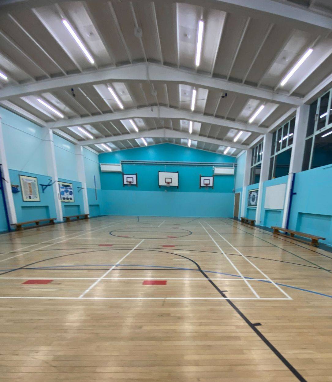 Indoor sports hall filming location in North Finchley Barnet N12, displaying marked court lines, blue walls, and high ceiling rafters from Love Locations.