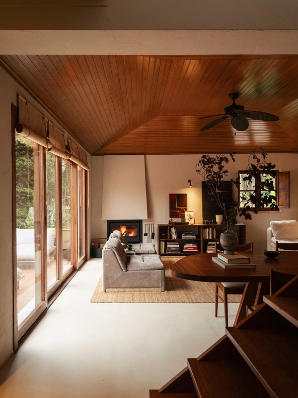 Sunlit rustic living room with sloped timber ceiling, sliding glass doors, and cozy fireplace nook, Love Locations 2705-064.