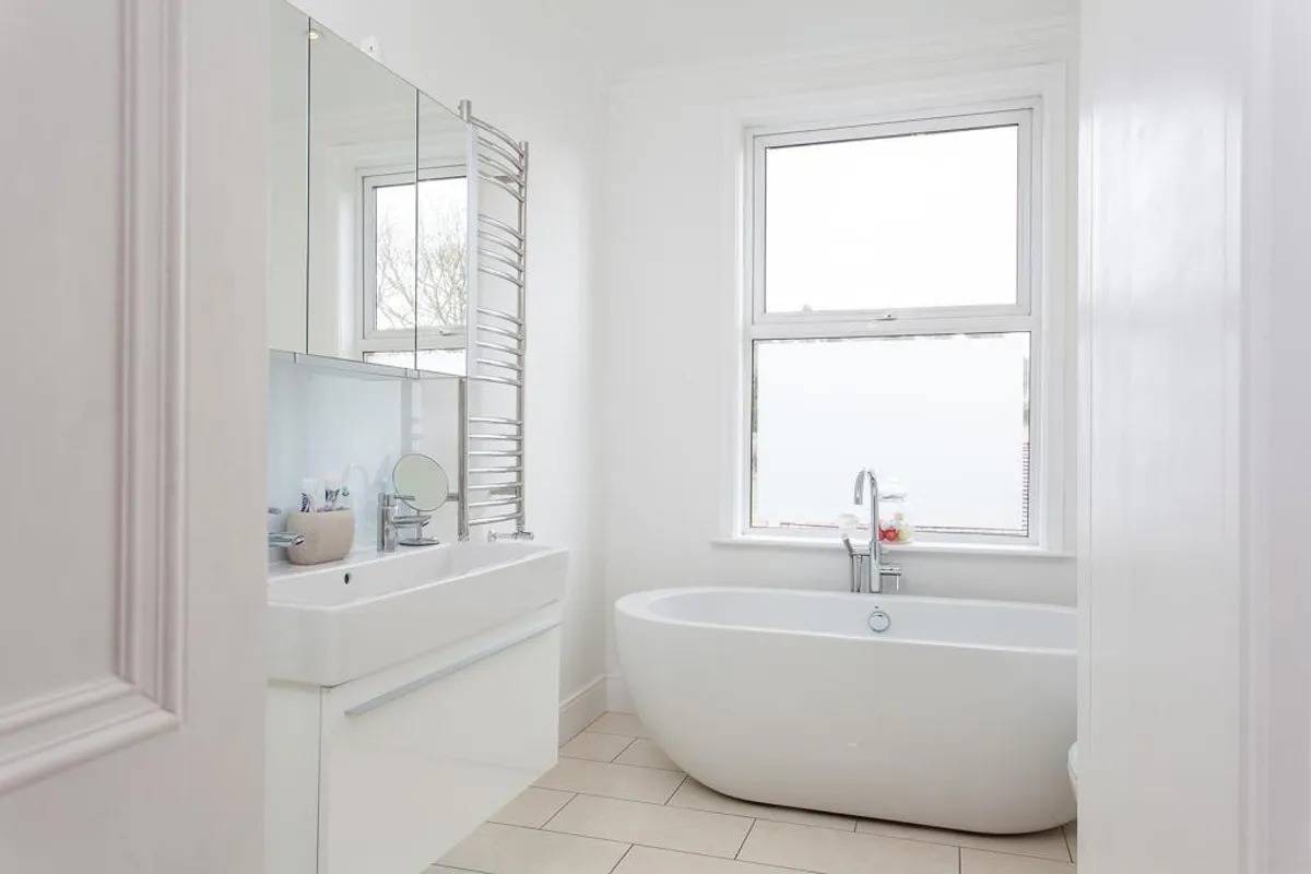 Contemporary white bathroom location house featuring a freestanding bathtub and sash window in Stockport SK6 through Love Locations.