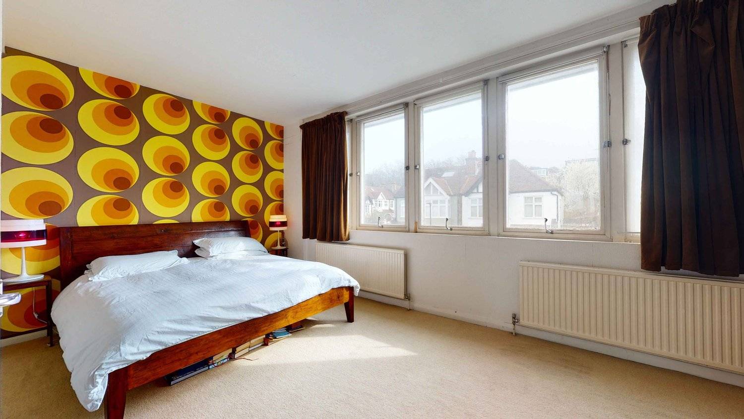 1970s retro bedroom featuring bold yellow and brown geometric floral wallpaper, low wooden bed, and wide windows, Love Locations SW16.