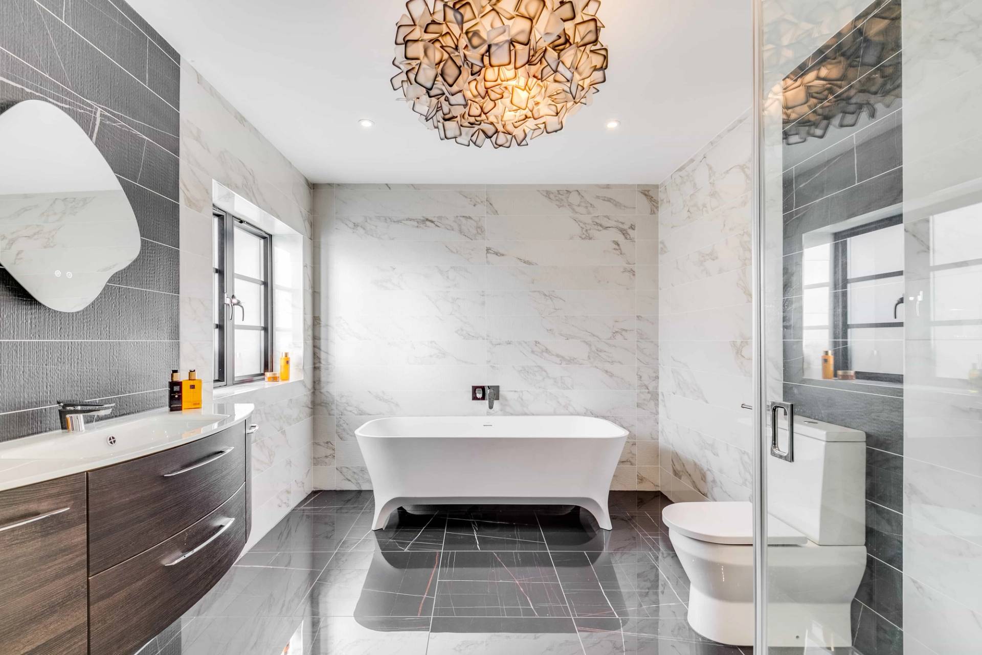 Luxury master ensuite featuring a white roll-top bathtub, dark marble floor tiles, and gold chandelier, Love Locations CB2.