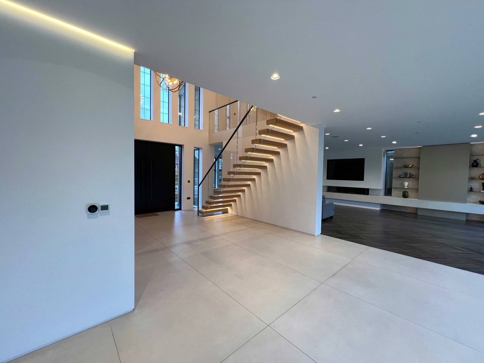 Double-height grand entrance hall with floating oak staircase, glass balustrade, and polished porcelain floor tiles, ideal for high-end production filming, Love Locations N3.