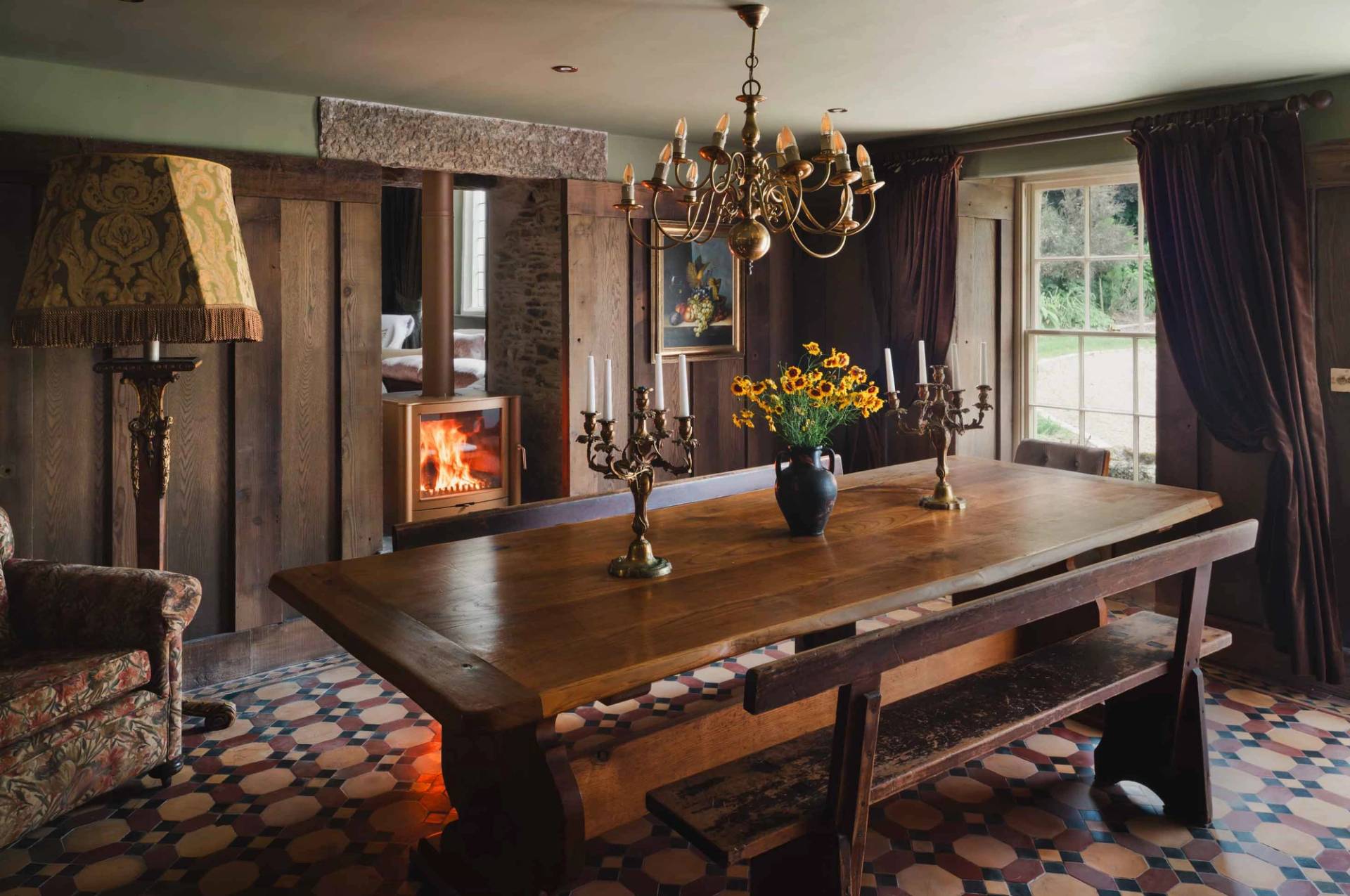 Atmospheric formal dining room film location in a Cornish manor house from Love Locations, featuring a long timber table, brass candelabra, and dark timber wall paneling.