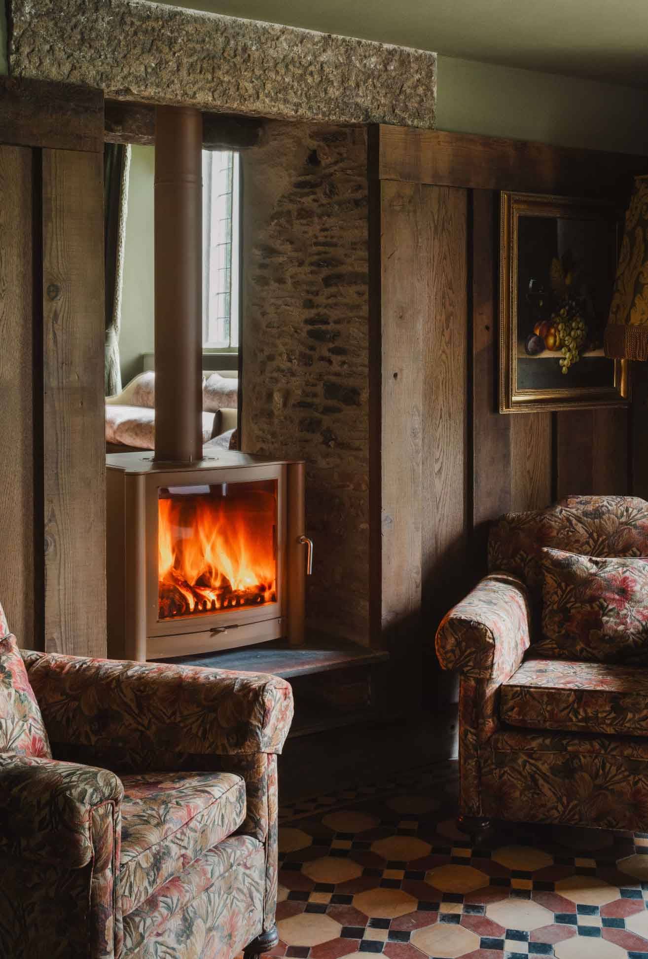 Wood-burning stove in a stone fireplace surround inside a panelled lounge in Newquay Cornwall TR8 by Love Locations.