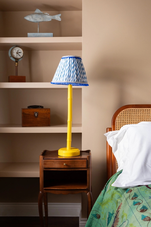Cozy bedroom interior available for film and photoshoot hire in Westminster SW1V via Love Locations, featuring a cane headboard bed next to an alcove shelf with a bright yellow lamp.