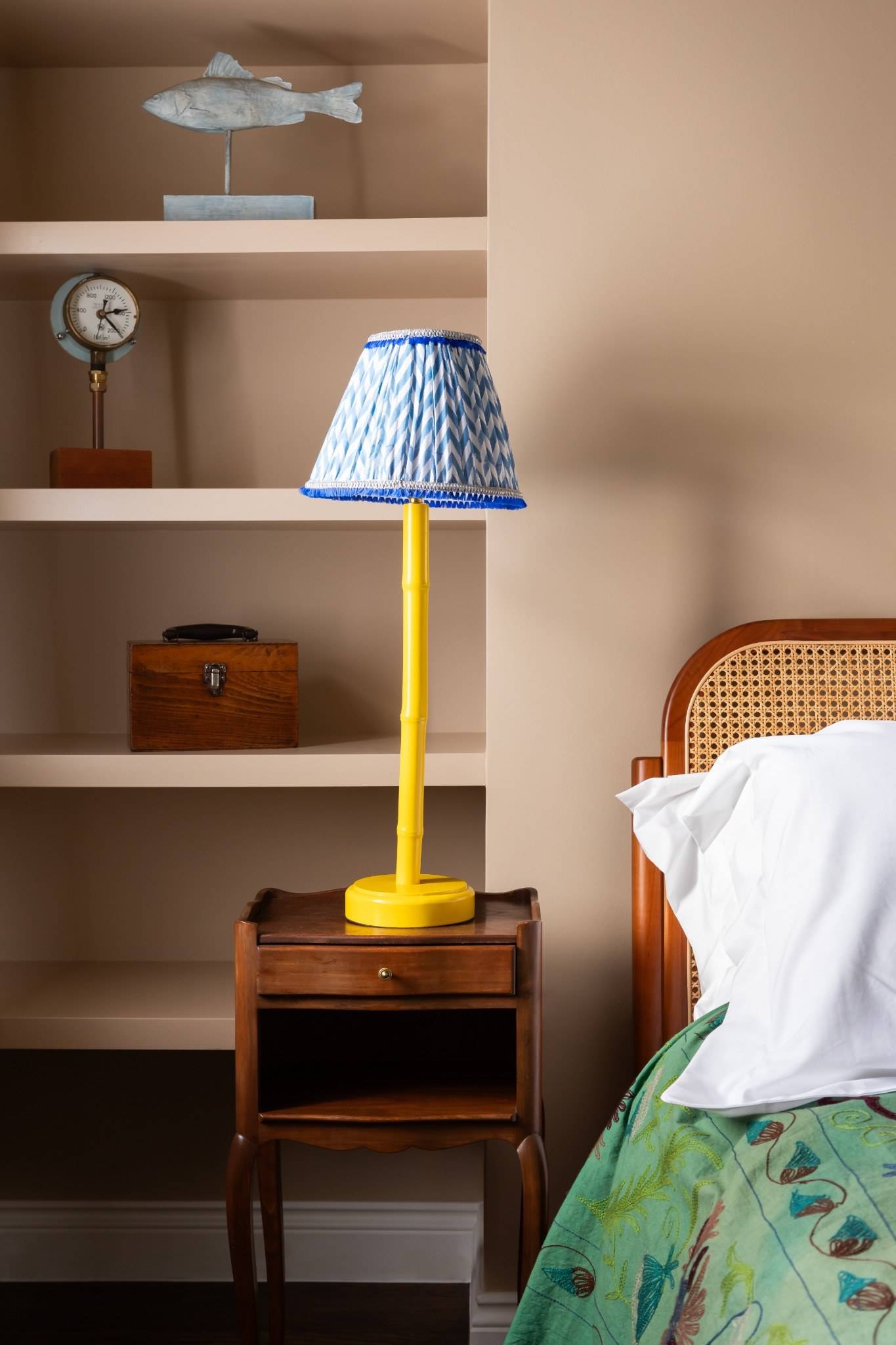 Cozy bedroom interior available for film and photoshoot hire in Westminster SW1V via Love Locations, featuring a cane headboard bed next to an alcove shelf with a bright yellow lamp.