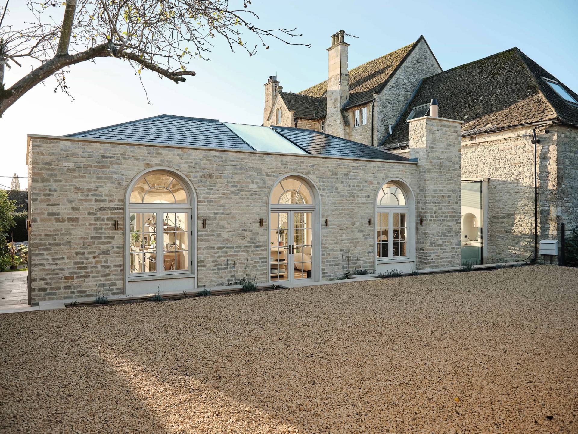 Exterior facade shot of a modern stone extension featuring arched glass doors, skylights, and a gravel driveway, ideal for automotive film shoots, Love Locations OX7.