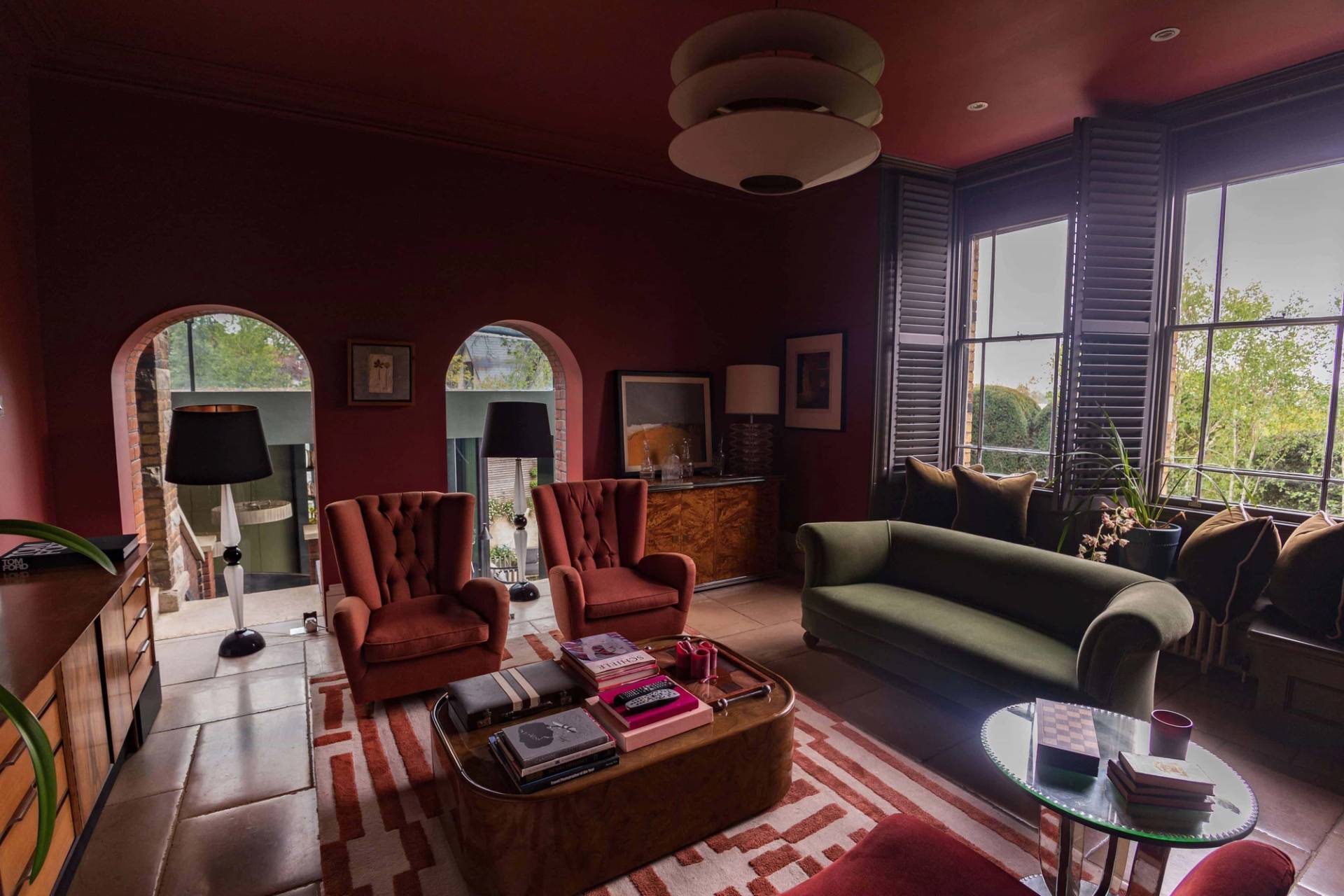 Rich red media room featuring orange velvet armchairs, dark green sofa, and arched windows, Love Locations.