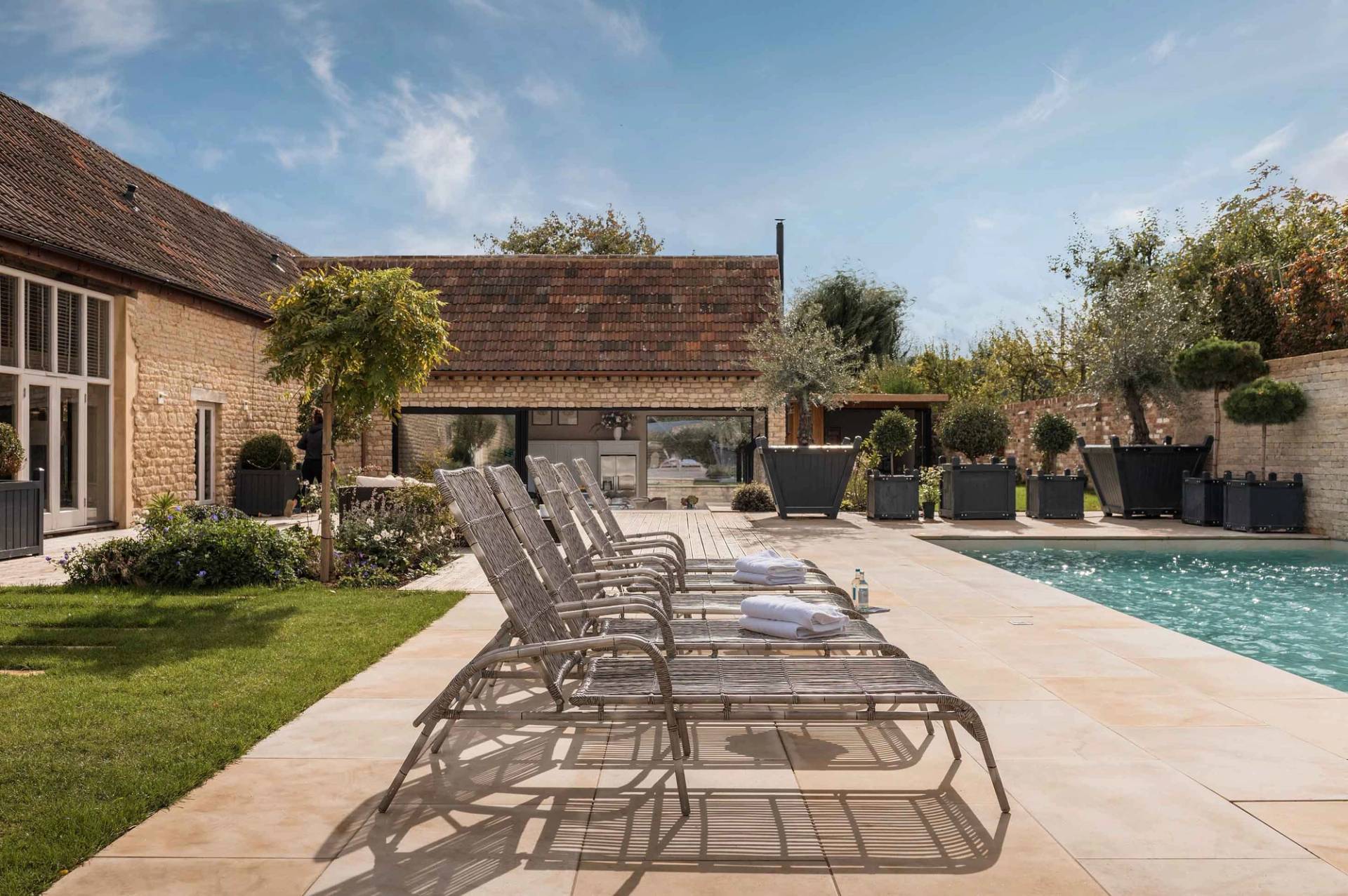 Row of sleek sun loungers on a paved stone terrace beside a luxury pool in Gloucestershire GL51 via Love Locations.