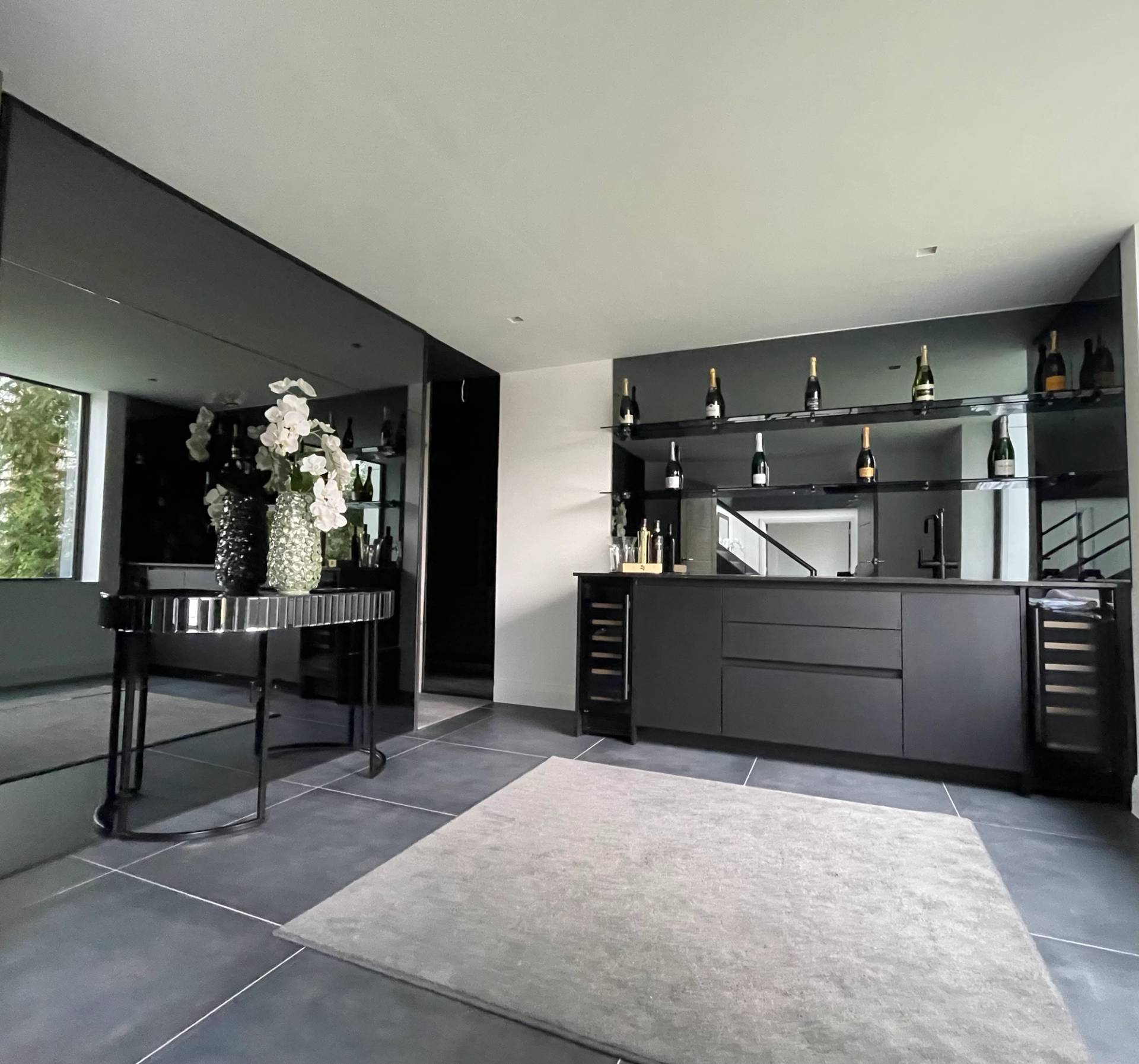 Modern home bar lounge featuring dark mirrored wall panels, console table, grey area rug, and garden views in Loughton, Love Locations IG10.