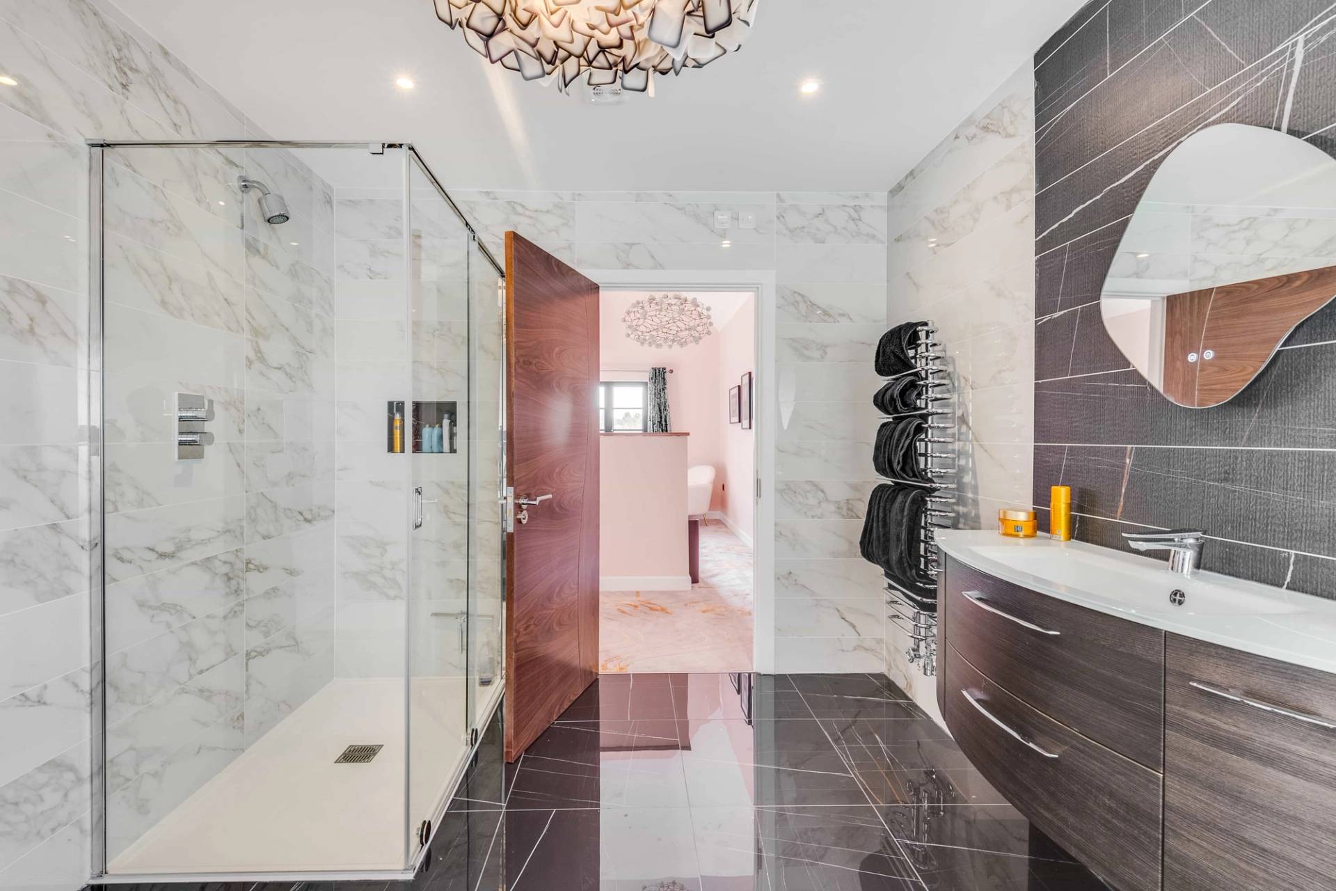 Ensuite bathroom with dark marble tile floors, glass shower enclosure, and floating vanity unit, Love Locations CB2.