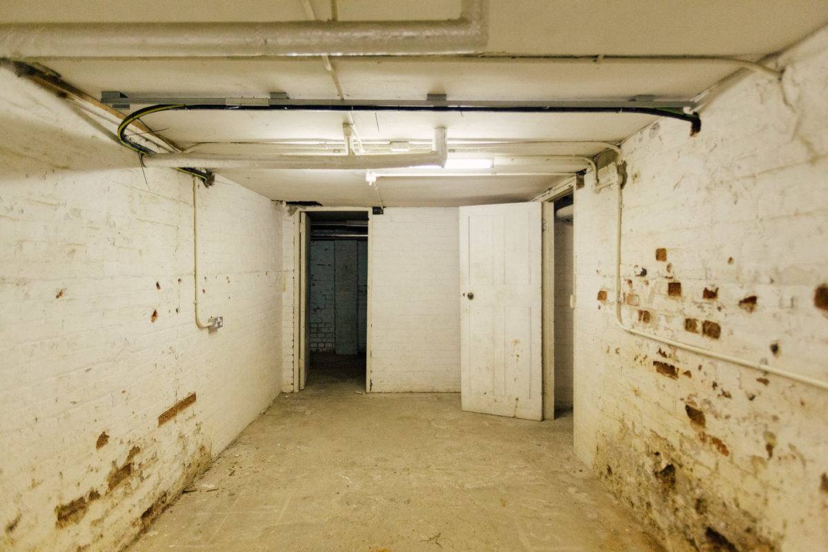 Raw brick basement room with white painted brickwork and rustic timber doors, perfect for film prop storage setups, Love Locations SE15.