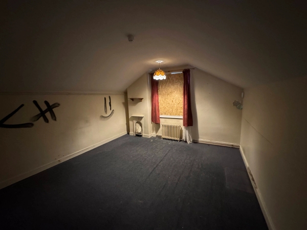 Dimly lit derelict bedroom with a small high window, deep red curtains, and dark carpets for horror films, Love Locations.