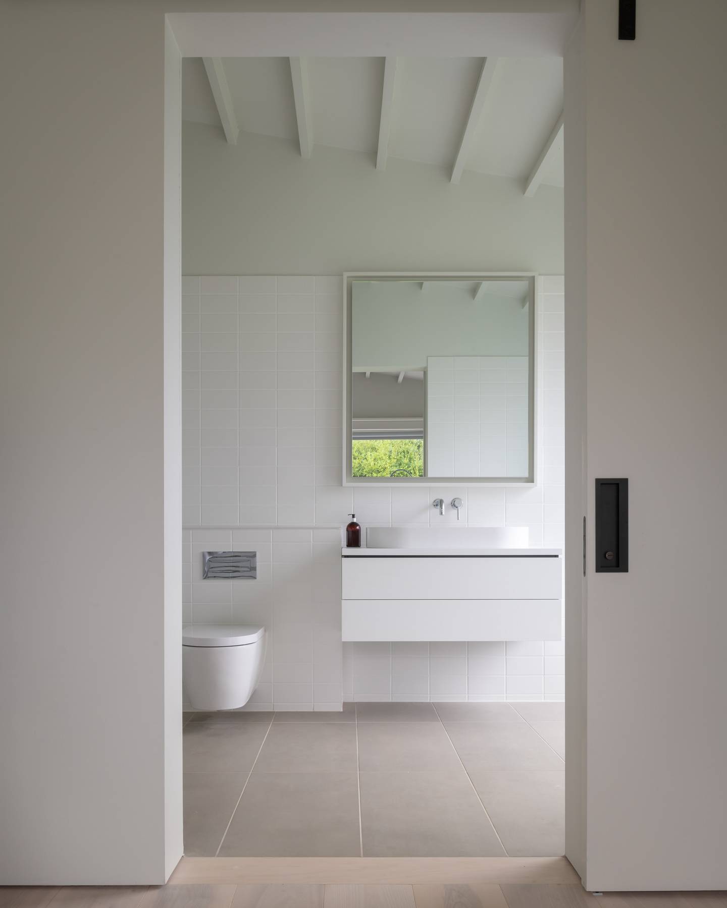 Minimalist guest bathroom with white vanity unit, floating toilet, and sliding privacy door, Love Locations BN3.