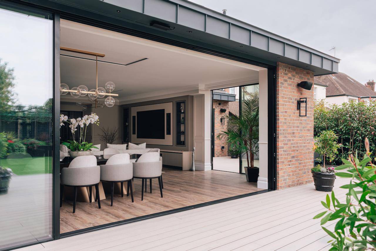 Wide-angle perspective from an outdoor deck through sliding glass doors into an open-plan luxury dining room, Love Locations W5.
