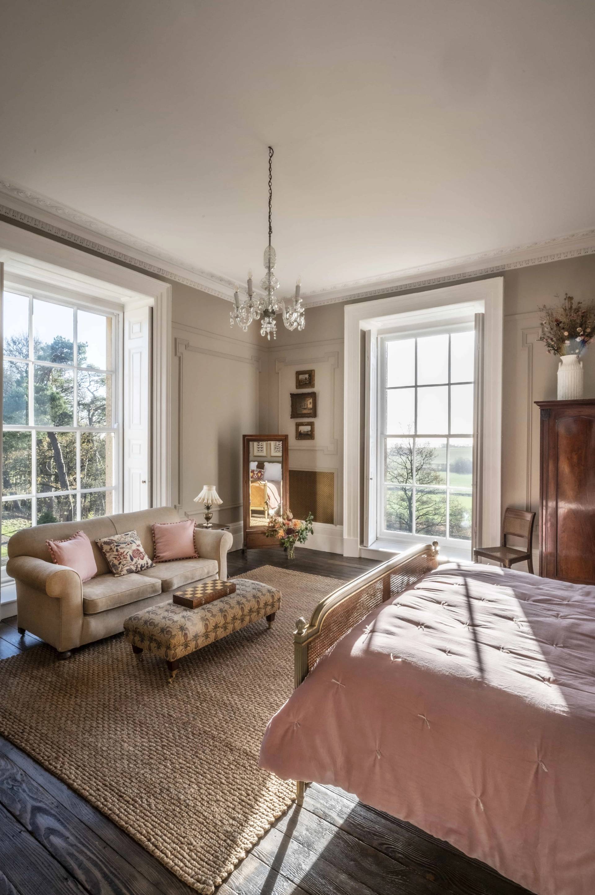Spacious master bedroom lounge area featuring a soft pink sofa, ottoman table, and large dual sash windows, Love Locations.