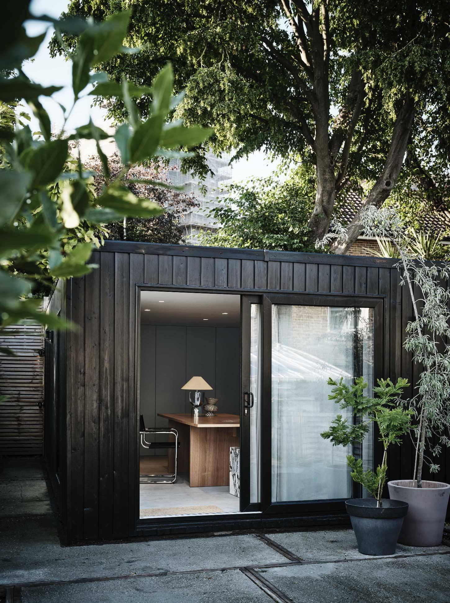 Black timber clad garden studio room in Waltham Forest, E4 with sliding glass doors opening onto a paved patio, Love Locations.