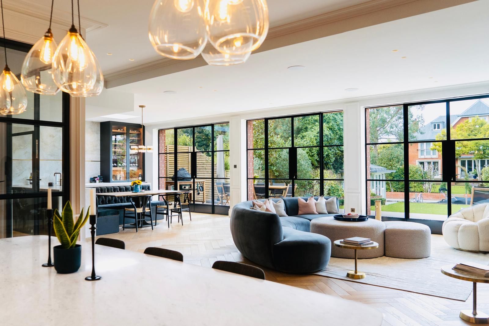 Modern double-fronted Victorian home open-plan living shoot location hero cover image in Teddington, TW11 featuring black steel Crittall glass patio doors, curved grey sectional sofa, marble kitchen island, banquette dining nook, herringbone oak floors, and glass pendant light fixtures, the ultimate high-visibility backdrop for TV drama filming, commercial brand campaigns, culinary productions, and interior design editorials via Love Locations.
